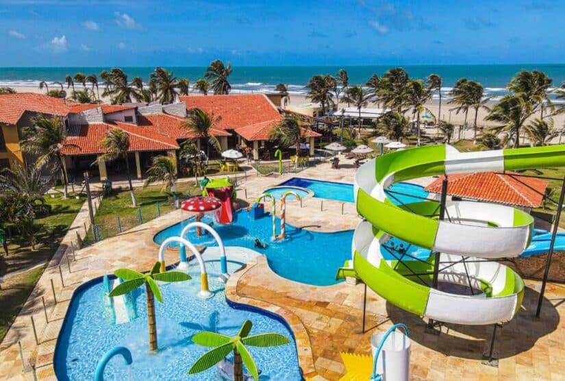 Vista aérea de um parque aquático à beira-mar com piscinas, escorregadores e palmeiras perto do oceano mostrando onde ficar em Aquiraz.