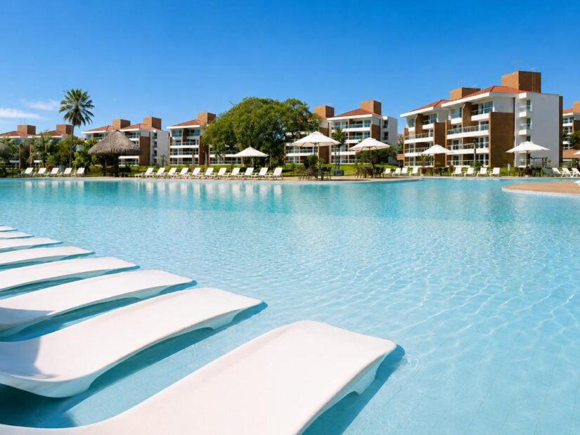 Catu Lake Resort no Ceará Espreguiçadeiras em uma piscina de resort, perfeita para onde ficar em Aquiraz perto do centro histórico, com guarda-sóis e edifícios modernos em um dia ensolarado.