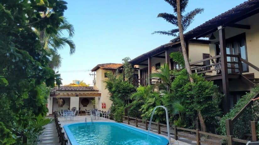 Pequena piscina externa cercada por vegetação onde ficar em Barra Grande Bahia, espreguiçadeiras e um prédio de dois andares com varandas.