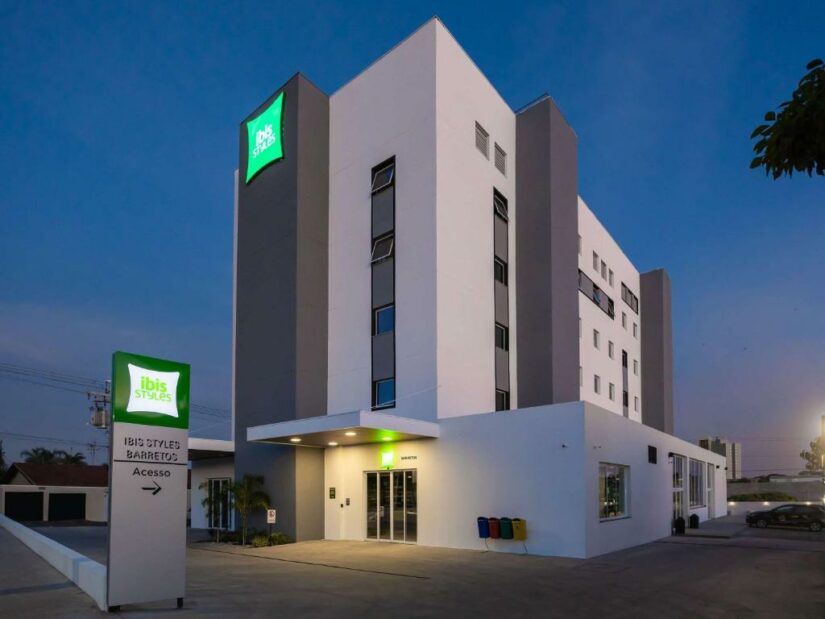Um moderno edifício do hotel Ibis Styles onde ficar em Barretos ao anoitecer, com uma entrada e sinalização iluminadas.