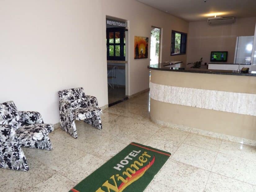 Saguão de hotel com uma recepção, duas cadeiras estampadas e um tapete com a inscrição Hotel Winner onde ficar em Barretos.