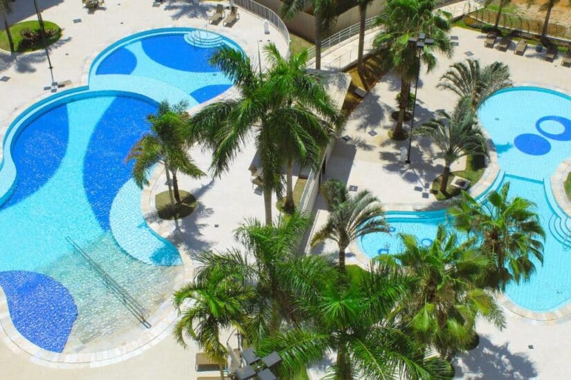 Vista aérea de duas piscinas em forma de Mickey Mouse cercadas por palmeiras e passarelas pavimentadas.