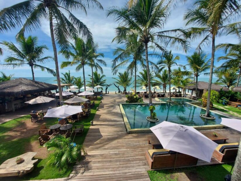 melhores pousadas à beira-mar na Bahia perto de Porto Seguro Piscina do resort com guarda-sóis e palmeiras - descubra onde se hospedar: onde ficar em Caraíva à beira-mar.