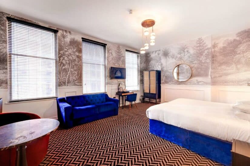 Quarto bem iluminado com carpete estampado, sofá e cama de veludo azul, móveis art déco e janelas grandes onde ficar em Liverpool.