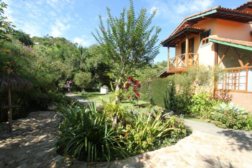 melhores pousadas perto de Nova Friburgo RJ Jardim exuberante com várias plantas ao lado de uma casa de dois andares - perfeito para quem procura onde ficar em Lumiar sob um céu azul.