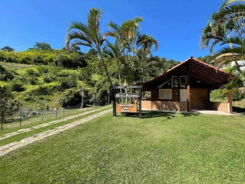 Uma pequena casa de tijolos com telhado vermelho e palmeiras, situada em um gramado com uma placa na frente.