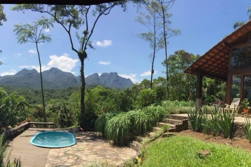 Pequena piscina e jardim ao lado de uma casa onde ficar em Morretes, com vista para a montanha e árvores verdes exuberantes sob um céu azul.