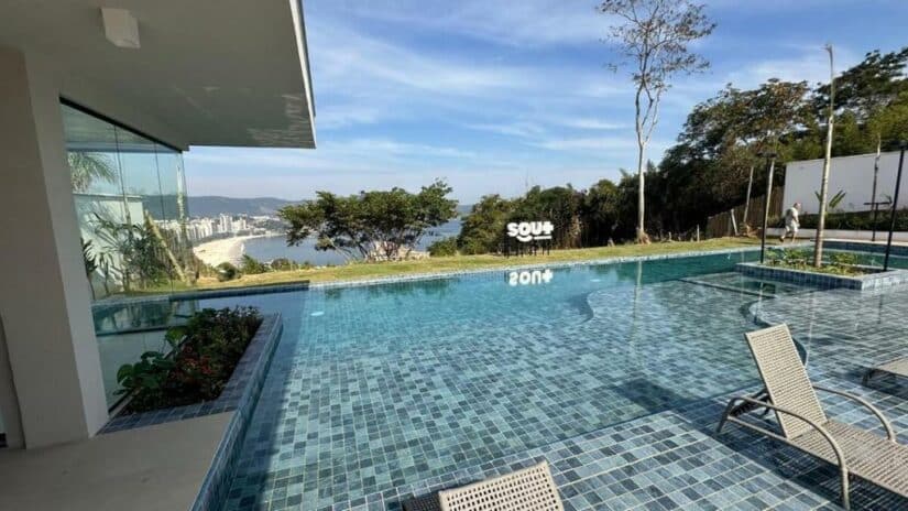 Piscina infinita com espreguiçadeiras, com vista para a cidade costeira e o oceano sob um céu azul claro mostrando Onde ficar em Niterói