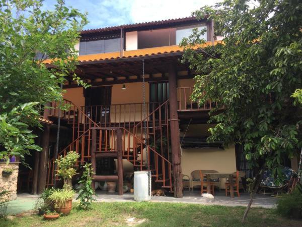 Casa de dois andares com uma varanda de madeira, vegetação, assentos ao ar livre e vasos de plantas no quintal.