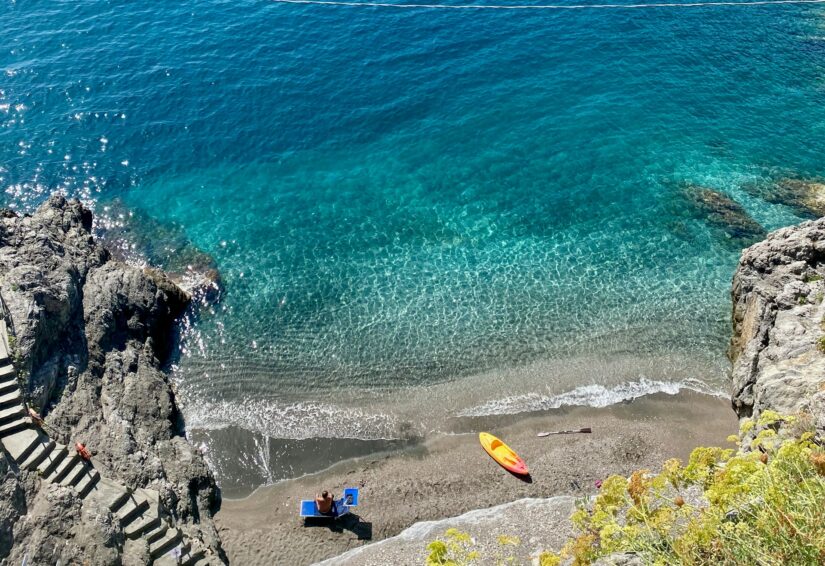 melhores hotéis em Maiori e Minori na Itália Vista aérea de onde ficar na Costa Amalfitana em Maiori e Minori: praia rochosa, água azul clara, caiaque amarelo e banhistas em toalhas.