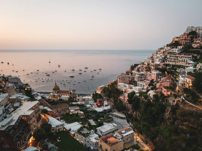 melhores hotéis em Positano Uma cidade litorânea de Positano com prédios coloridos em uma colina - perfeita para decidir onde ficar na Costa Amalfitana ao pôr do sol.