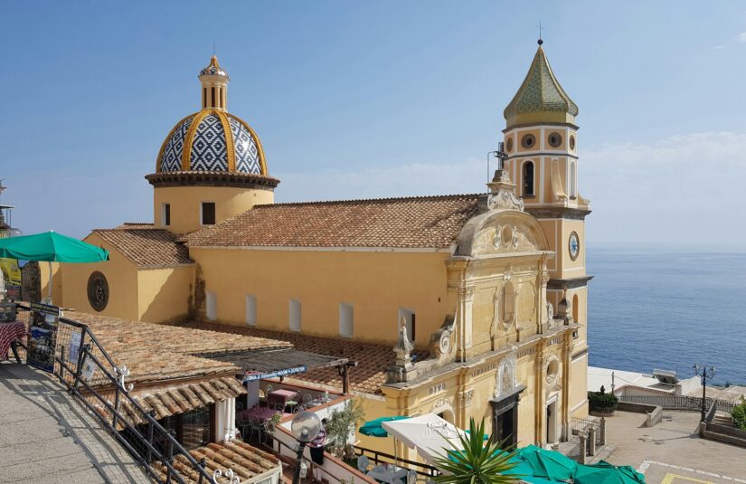onde ficar na Costa Amalfitana em Praiano e Conca dei Marini Uma igreja amarela com uma cúpula de azulejos coloridos tem vista para o mar - uma vista icônica de de Praiano e Conca dei Marini na Itália