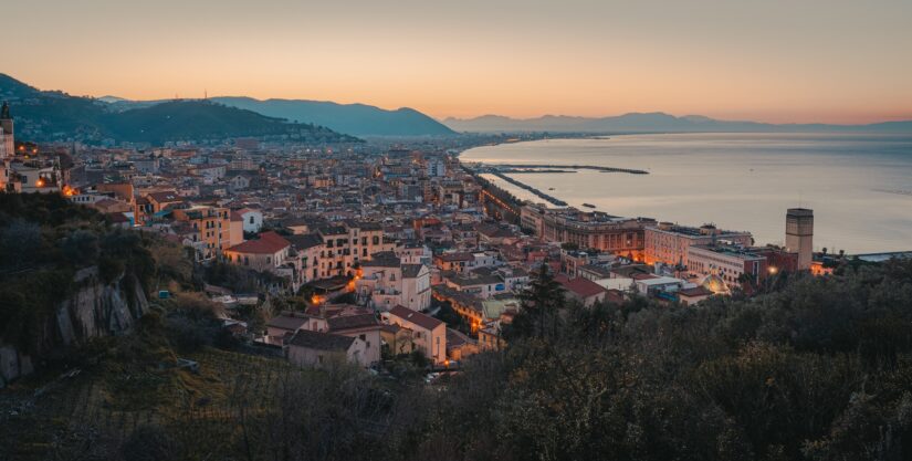 onde ficar na Costa Amalfitana em Salerno e Sorrento Paisagem urbana litorânea de Salerno e Sorrento ao pôr do sol com montanhas, edifícios em um mar calmo.