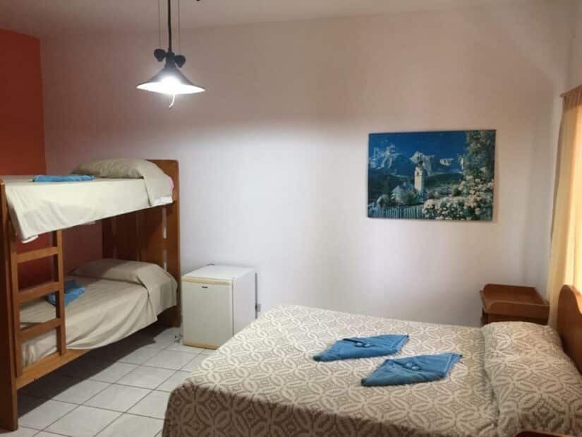 Um quarto aconchegante com uma cama de casal, beliches, frigobar e um quadro na parede.