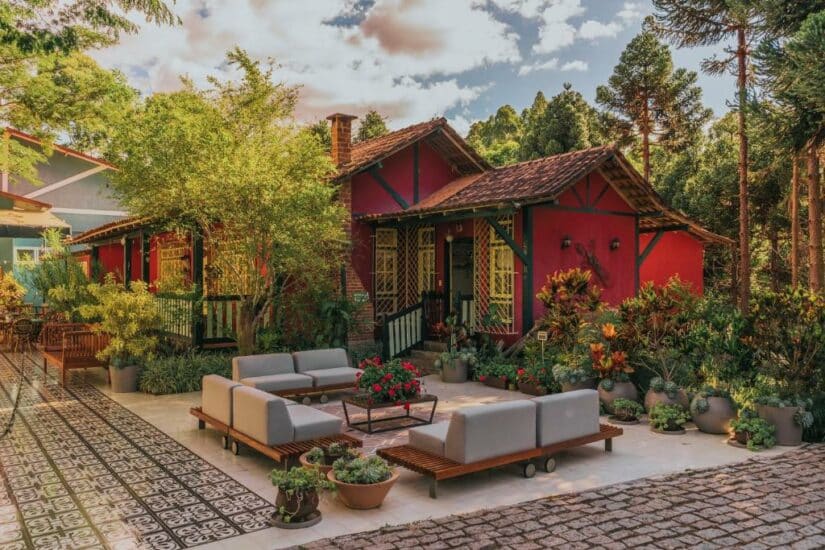 Uma casa vermelha com telhado de telhas, jardim exuberante e modernos assentos ao ar livre em um dia ensolarado.