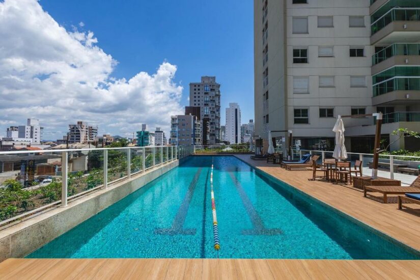 Piscina externa na cobertura com edifícios da cidade ao fundo em um dia ensolarado.