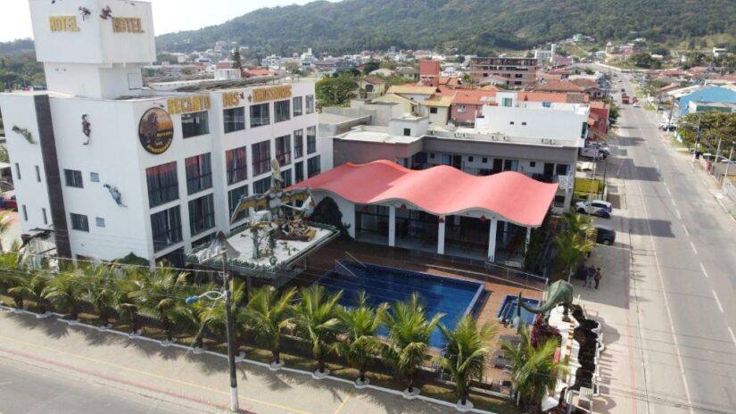 Vista aérea de um hotel onde ficar em Penha, cobertura vermelha, palmeiras e ruas ao redor em uma cidade costeira.