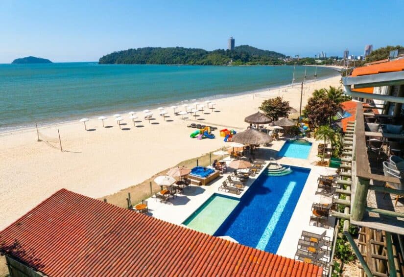 Um resort à beira-mar onde ficar em Penha com piscina, espreguiçadeiras, guarda-sóis e uma praia de areia à beira do oceano azul.