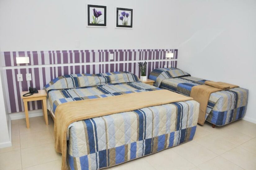 Quarto de hotel onde ficar em Penha com duas camas, colchas listradas, mesinhas de cabeceira, arte na parede e uma parede de destaque listrada.