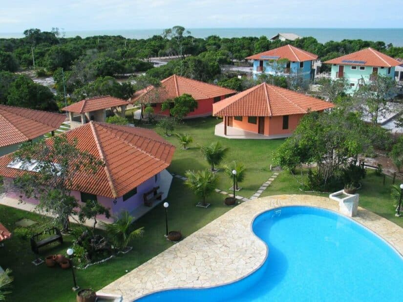 Vista aérea de um resort onde ficar em Prado com piscina, gramados verdes e várias vilas com telhado vermelho perto do oceano.