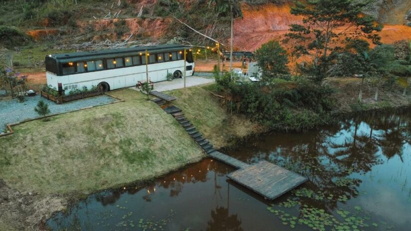 Um ônibus convertido estacionado em uma lagoa com um cais de madeira e escadas que levam à água.