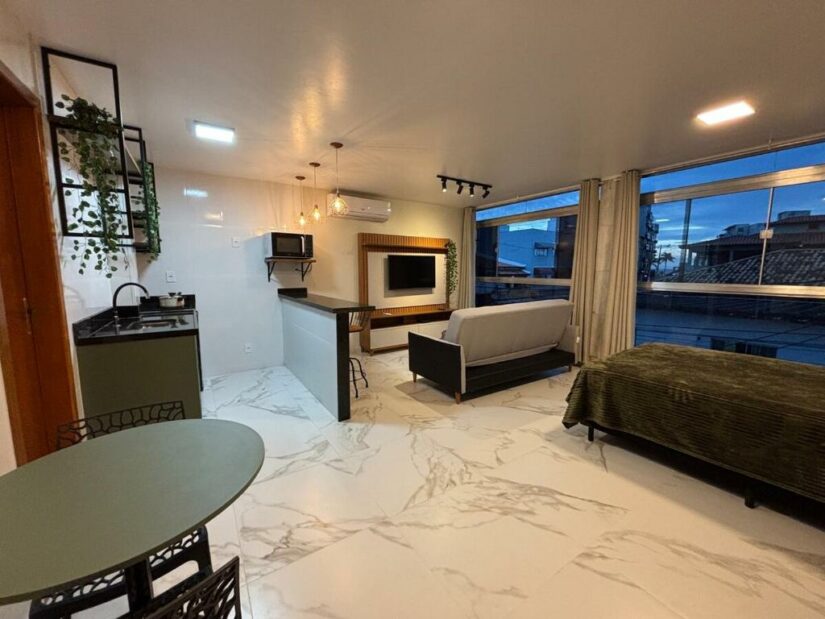 Apartamento estúdio moderno com piso de mármore, janelas grandes, cozinha, sofá e mesa de jantar.