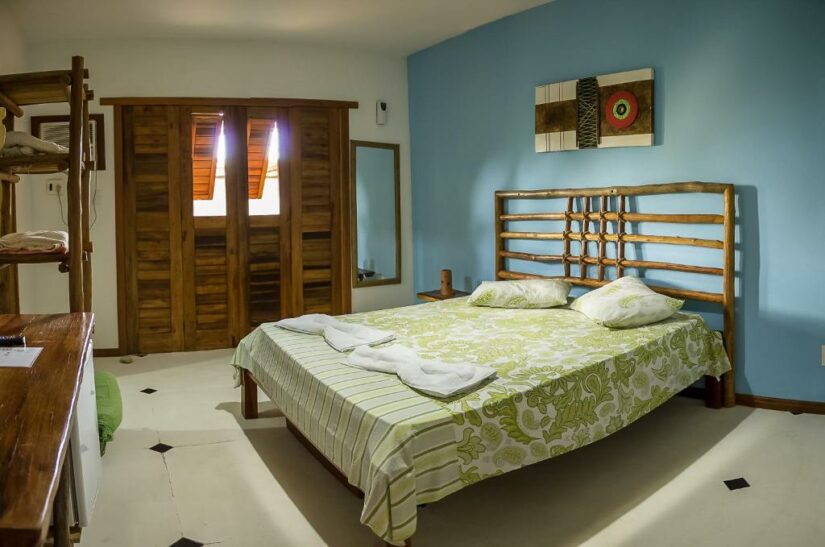 Quarto aconchegante Onde ficar em Taipu de Fora com cama de madeira, roupa de cama verde, parede de destaque azul e portas de armário de madeira.