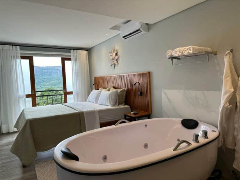 Quarto de hotel onde ficar em Tiradentes moderno com uma cama, banheira, varanda com vista para a montanha e toalhas dobradas em uma prateleira.