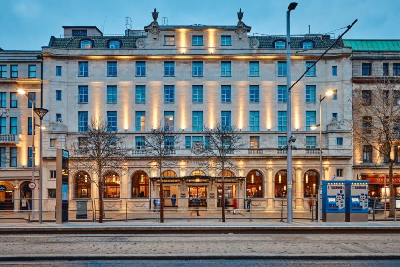 Um edifício grandioso onde ficar na Irlanda e bem iluminado com janelas em arco e linhas de bonde na frente ao anoitecer.