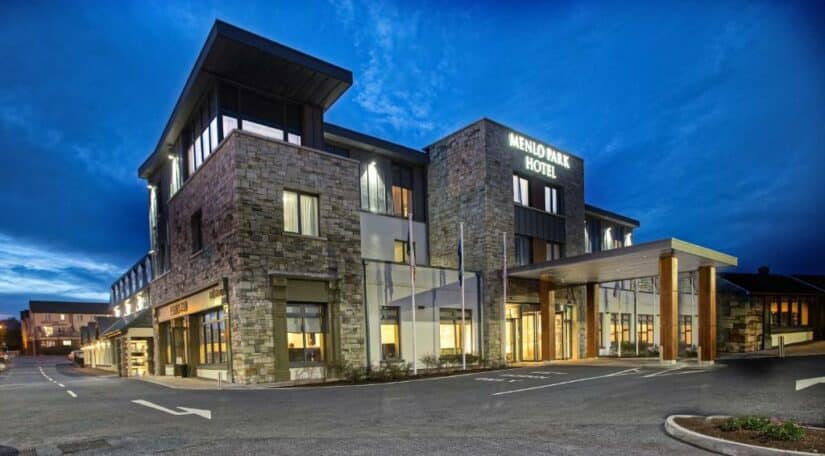 Edifício moderno de pedra do Menlo Park Hotel ao anoitecer, com janelas e entrada iluminadas.