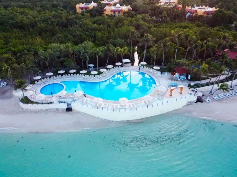Vista aérea da piscina de um resort à beira-mar onde ficar na Riviera Maya, cercada por árvores, com espreguiçadeiras e mar azul-turquesa.