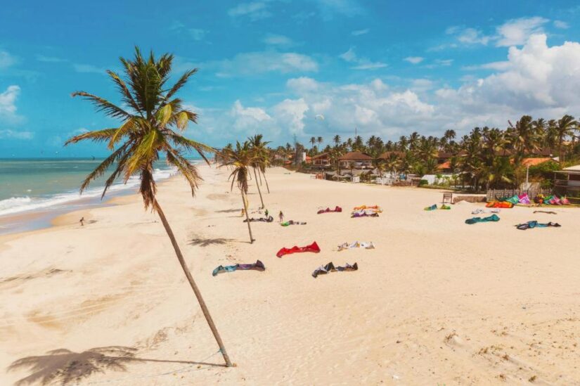 Ampla praia de areia com palmeiras e pipas coloridas - explore onde ficar em Cumbuco sob o vibrante céu azul.