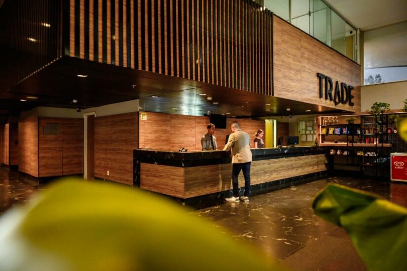 hotéis em cascatinha em juiz de fora MG Um homem está na recepção de um hotel moderno Onde ficar em Juiz de Fora com o nome TRADE, falando com dois funcionários.