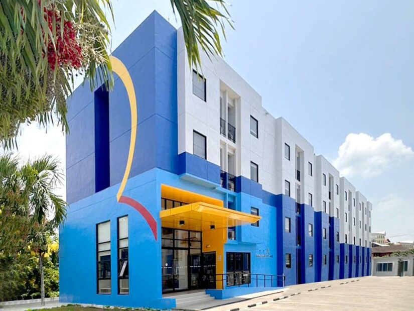 Edifício moderno onde ficar em Krabi em azul e branco com detalhes em amarelo, palmeiras e um céu claro ao fundo.