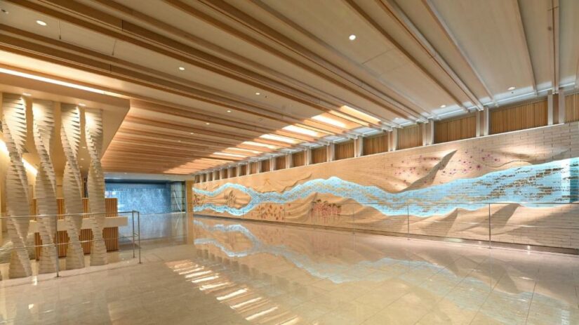 Um corredor moderno com piso refletivo e um grande mural artístico ondulado na parede à direita.