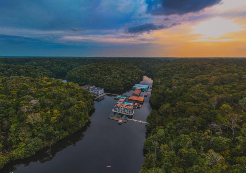 onde ficar em Manaus na Ponta Negra Vista aérea de um resort com edifícios no Rio Negro cercado pela Floresta Amazônica ao pôr do sol.