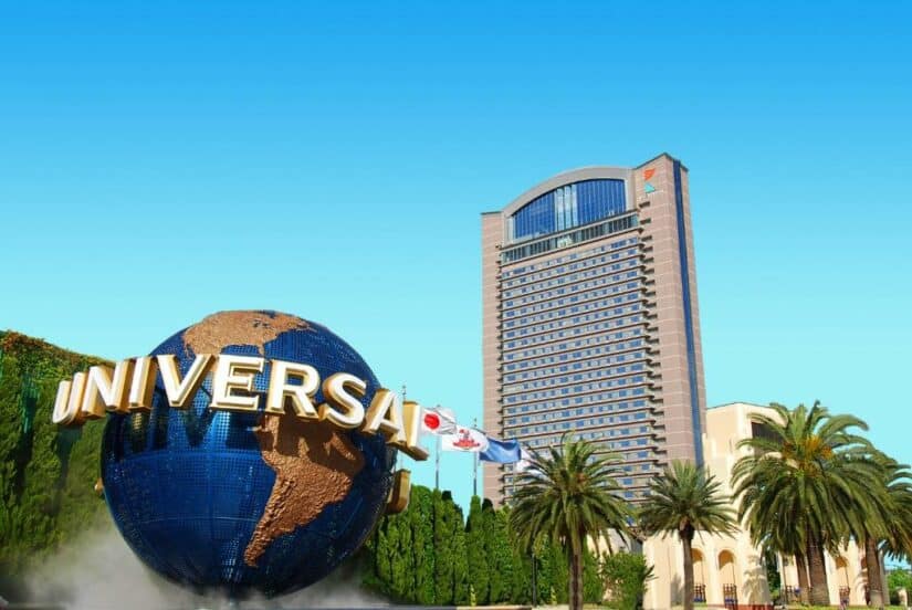 O globo do Universal Studios com bandeiras e um prédio alto de hotel  onde ficar em Osaka sob um céu azul claro.