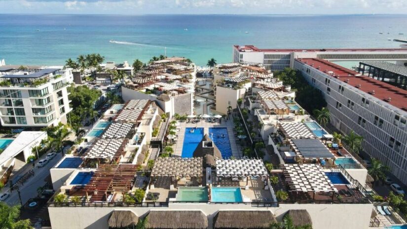 Vista aérea de um resort de luxo na praia com piscinas, cabanas e o oceano ao fundo.