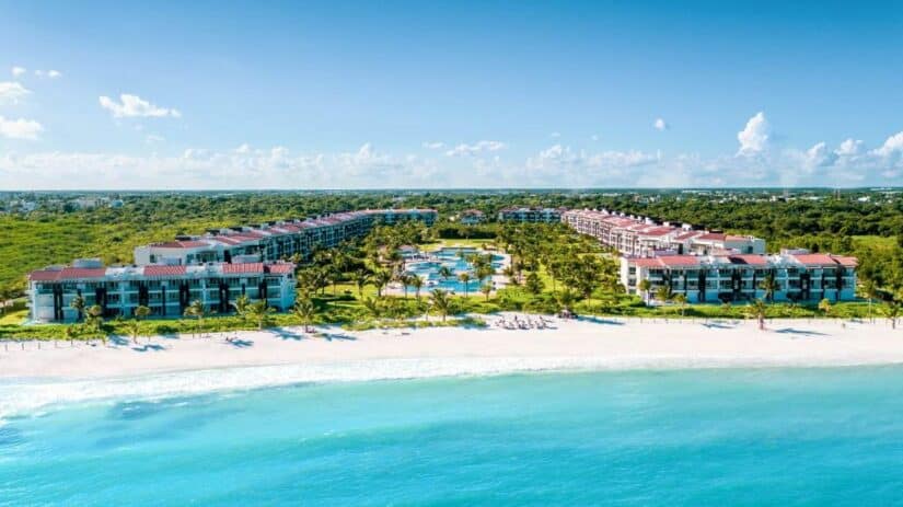 Vista aérea de um resort à beira-mar onde ficar em Playa del Carmen com piscinas, palmeiras e edifícios voltados para o oceano azul-turquesa.