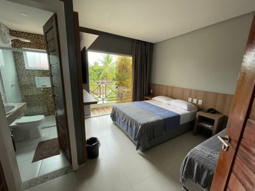 Um quarto de hotel moderno com uma cama de casal, uma varanda e um banheiro privativo, com vista para a vegetação externa.