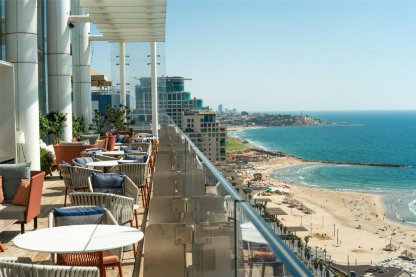 Terraço na cobertura Onde ficar em Tel Aviv com assentos com vista para a praia de areia e o mar azul em um dia ensolarado.