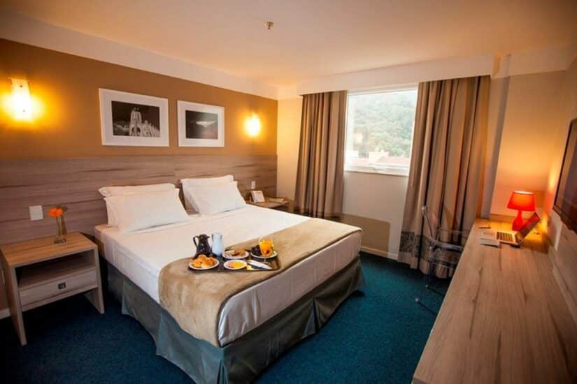 Um quarto de hotel moderno com uma cama de casal, bandeja de café da manhã, escrivaninha e janela com vista panorâmica.