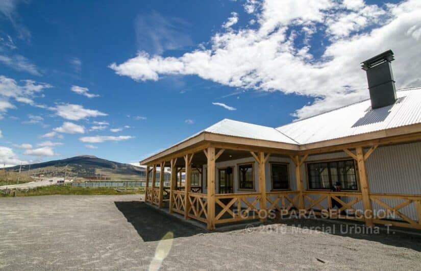 Uma casa de madeira onde ficar em Torres del Paine com uma varanda envolvente sob um céu azul brilhante com nuvens dispersas.