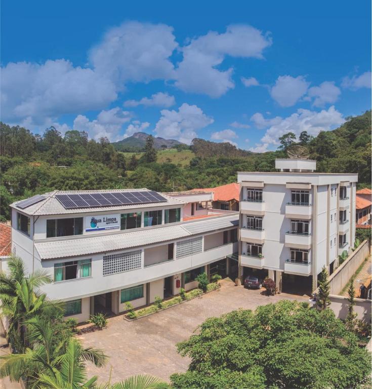 onde ficar em Bichinho MG Um edifício branco de vários andares com painéis solares, cercado por árvores e colinas sob um céu azul com nuvens.