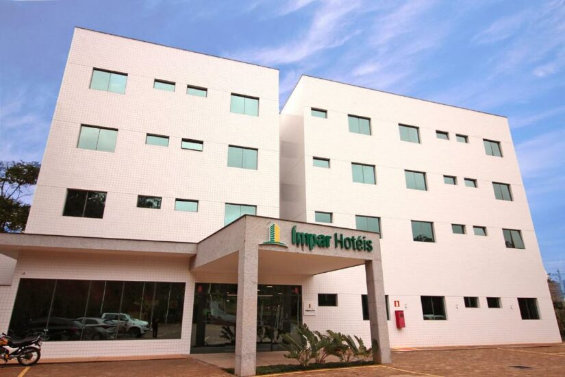Um moderno edifício de hotel branco onde ficar em Catas Altas com janelas verdes e a placa Impar Hotéis acima da entrada.