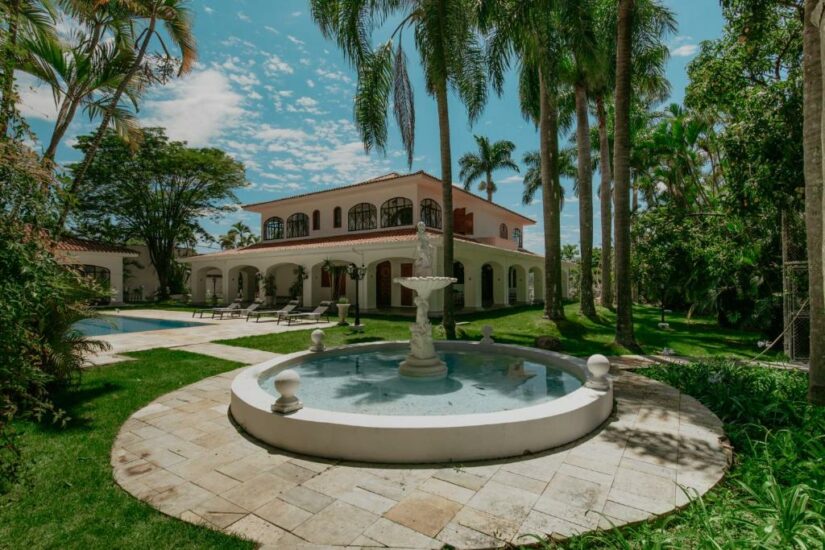 hotéis em Espírito Santo do Pinhal em SP Uma fonte redonda fica em frente a uma grande casa de dois andares onde ficar em Espírito Santo do Pinhal cercada por palmeiras e vegetação exuberante.