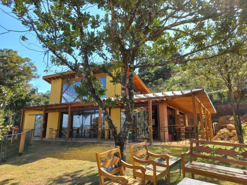 onde ficar em Espírito Santo do Pinhal interior de São Paulo Uma casa amarela com janelas grandes, pátio de madeira, mesas ao ar livre e árvores em um quintal verde e ensolarado.