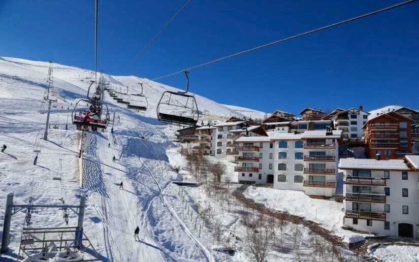 hotéis em La Parva perto de Farellones no Chile Teleférico de esqui subindo uma montanha nevada perto de modernos edifícios alpinos onde ficar em Farellones sob um céu azul claro.