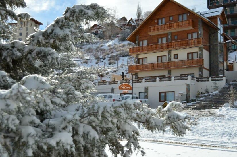 hotéis na Vila de Farellones no Chile Uma árvore coberta de neve em frente a um alojamento de madeira e casas em uma encosta nevada onde ficar em Farellones.