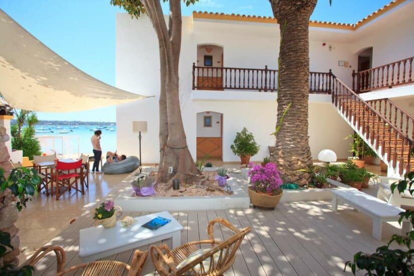 hotéis em La Savina em Formentera perto de Ibiza na Espanha Pátio ensolarado com palmeiras, espreguiçadeiras e vista para o mar; as pessoas relaxam perto da água onde ficar em Formentera.